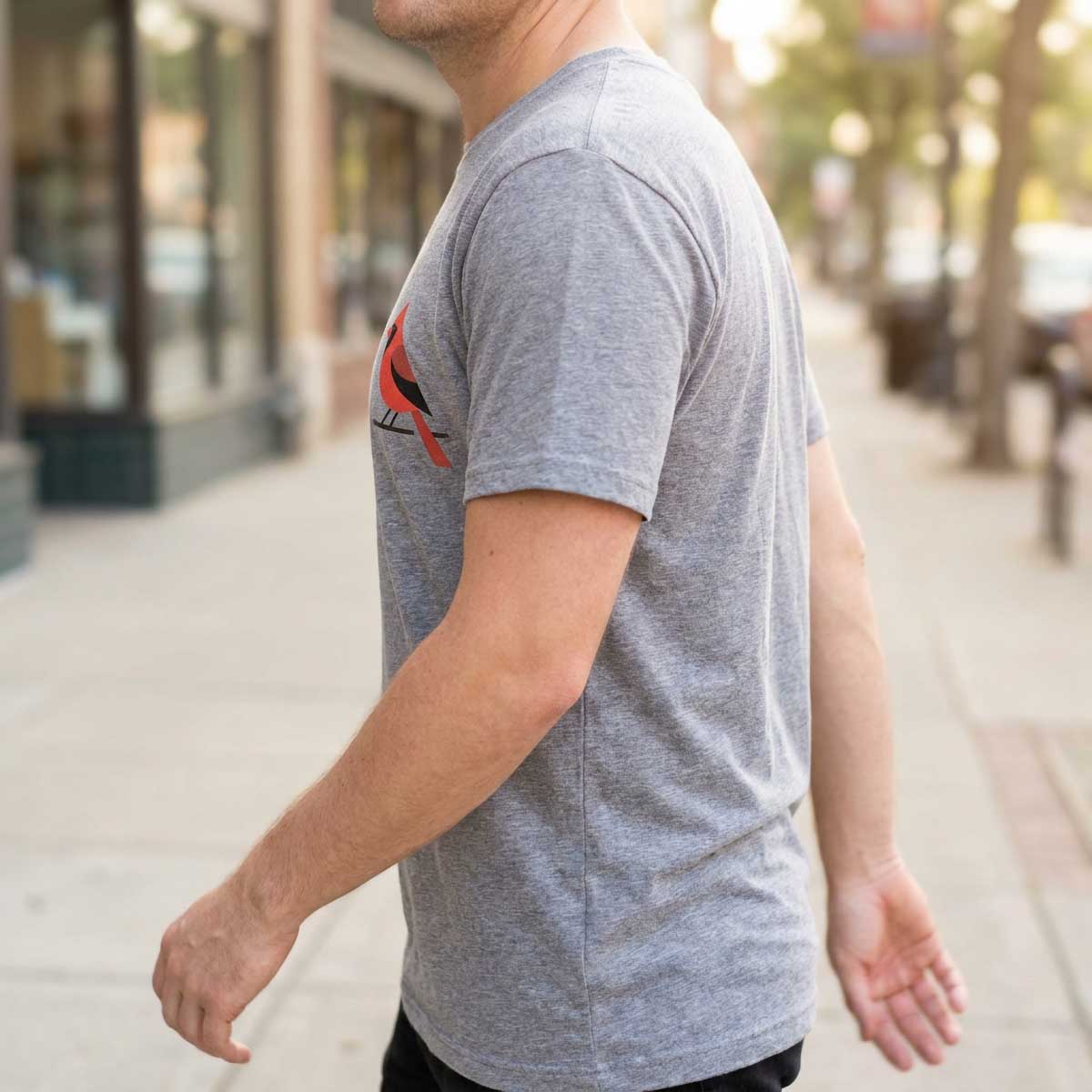 Person walking on a sunlit pavement, small cardinal print on left chest