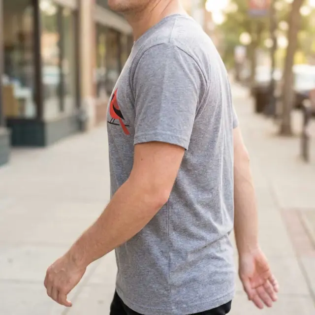 Person walking on a sunlit pavement, small cardinal print on left chest