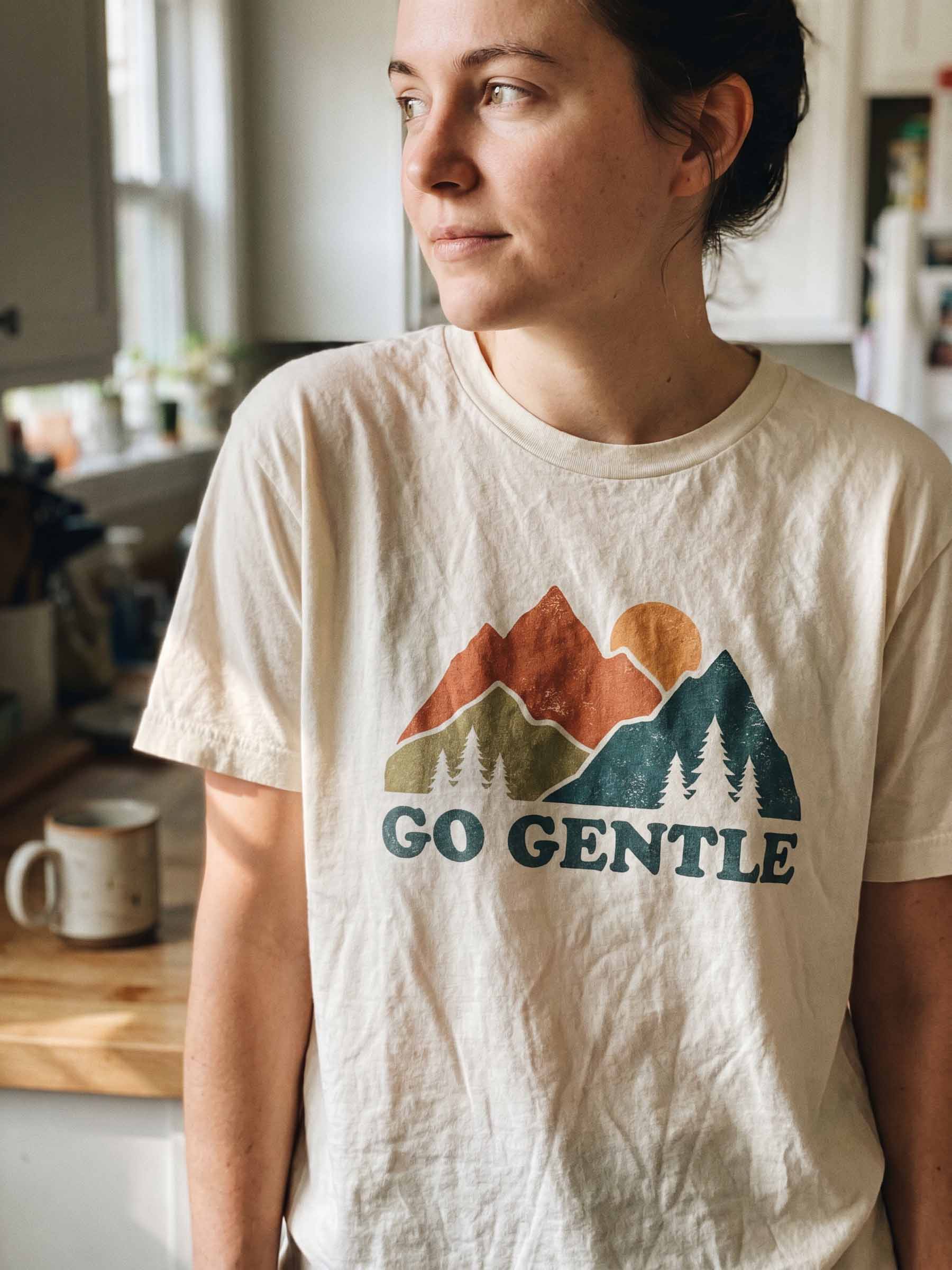 Candid kitchen photo of a person wearing a cream Go Gentle mountain-print t-shirt